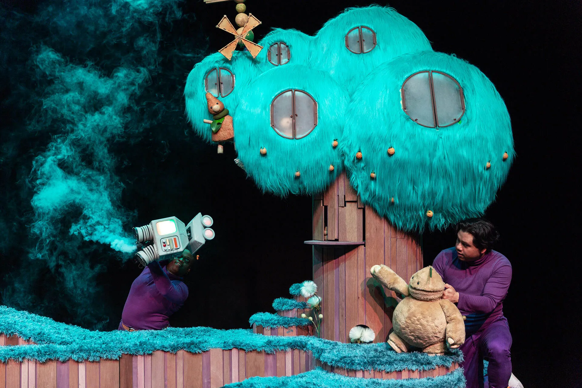 Beep the robot and Mort on stage in a colourful village setting.